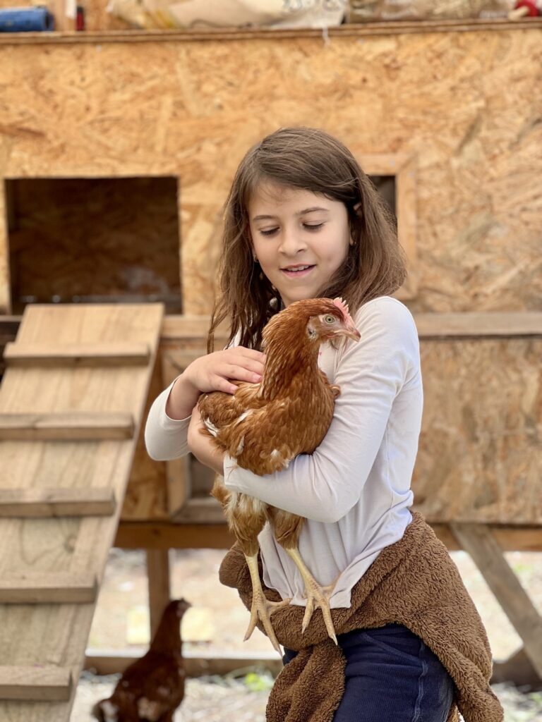 Niña cuidando una gallina en el espacio exterior de Natura Montessori School